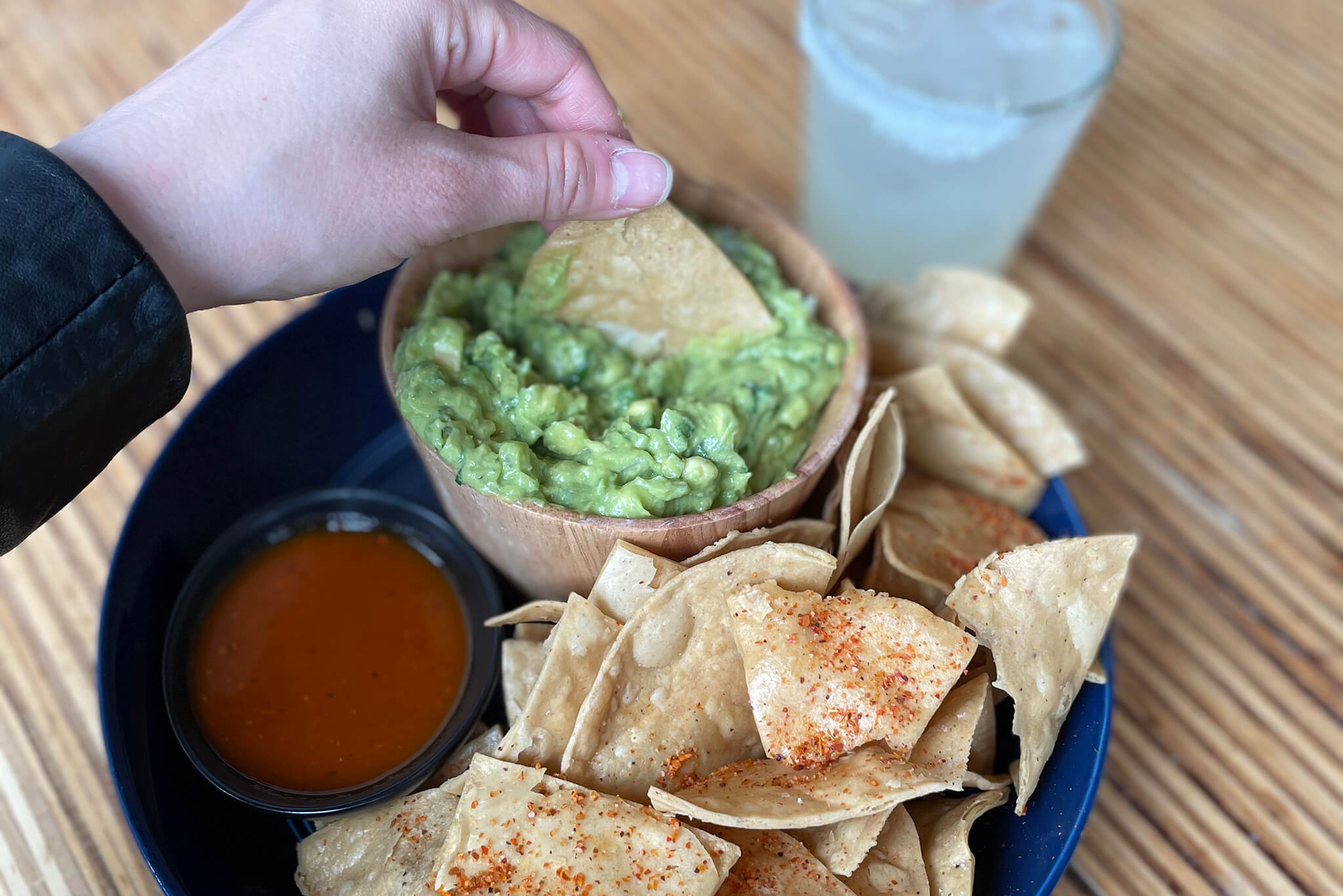 Photo of a hand dipping chips into guacamole